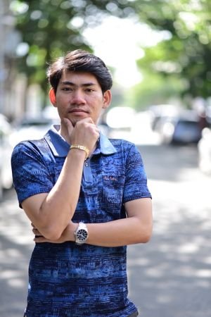 Young man in a blue polo shirt posing thoughtfully outdoors on a sunny day.